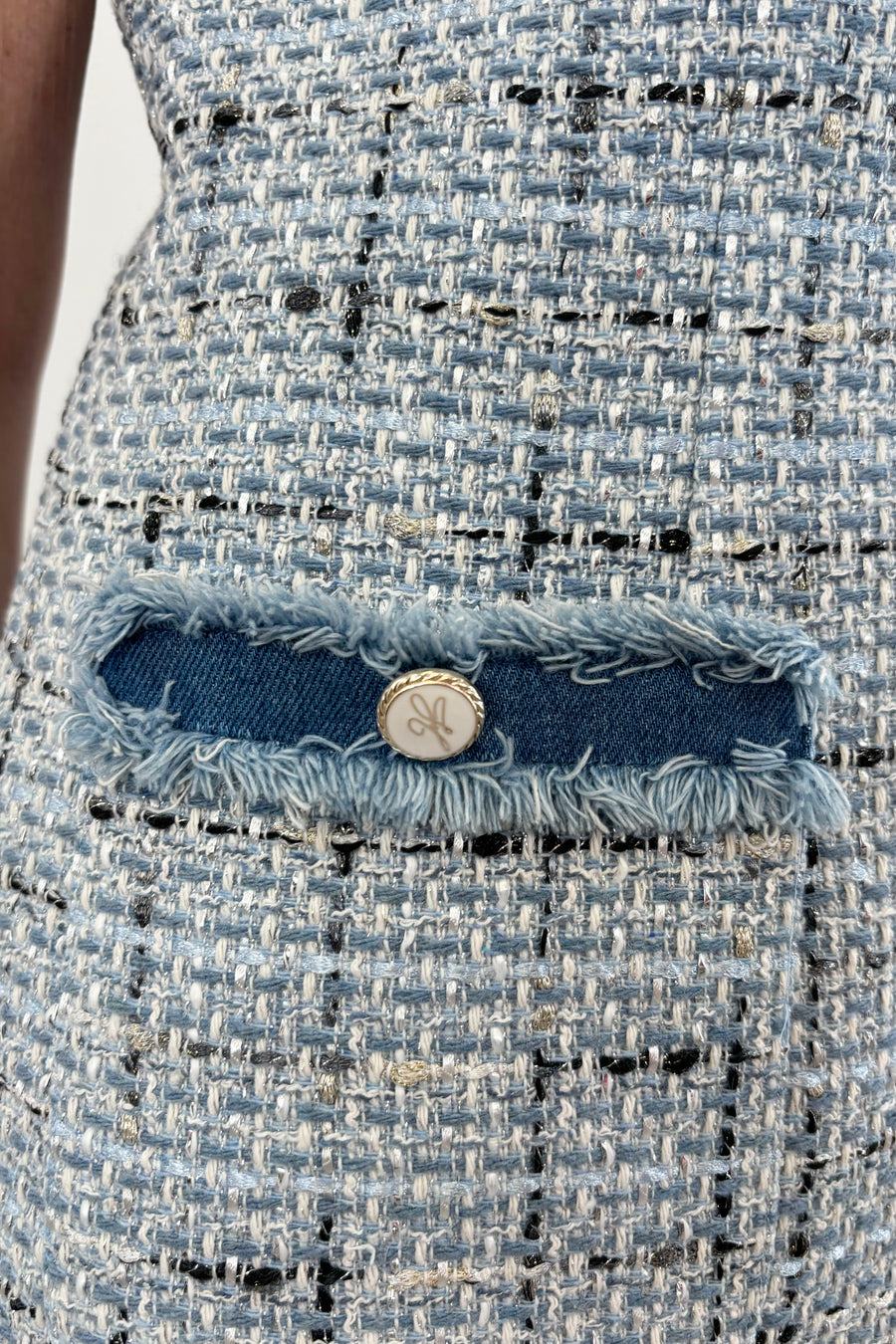 Close up of detail pocket on woman wearing sleeveless blue tweed short dress with denim trim and two front pockets