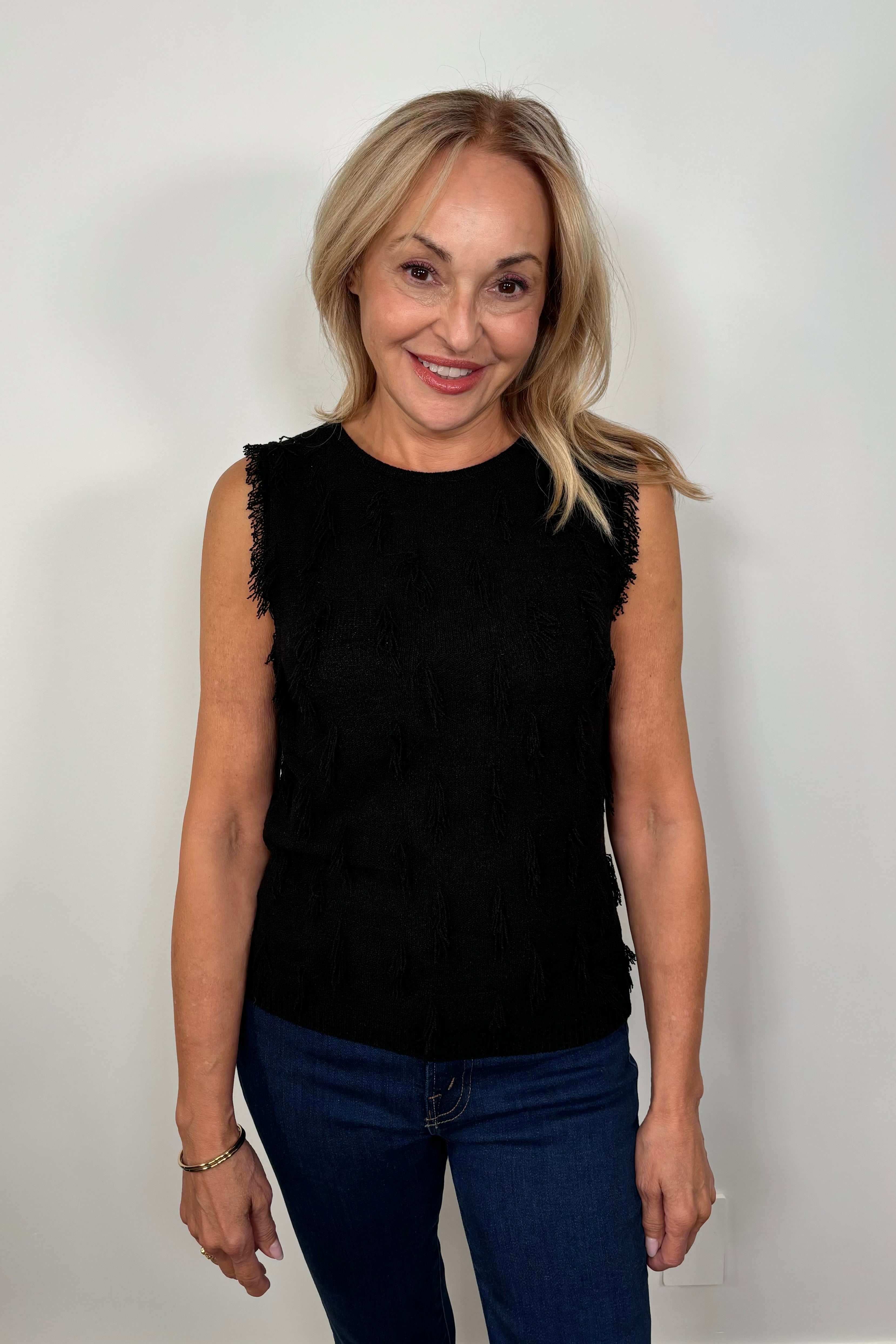 Front view of a woman wearing a black tank top with fine gauge fringes 