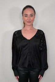 woman wearing a black long sleeve satin blouse with lace detailing on the shoulders untucked 