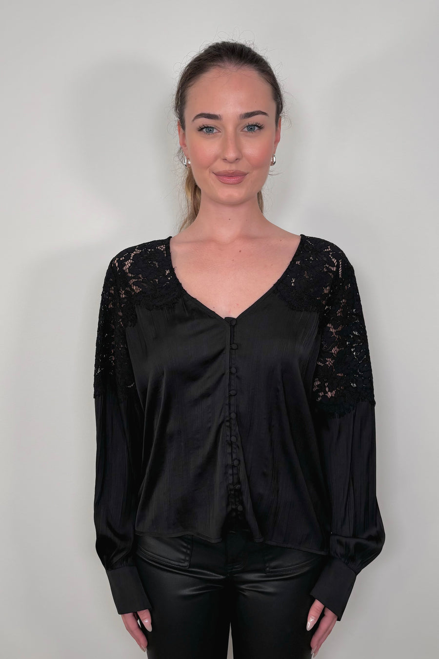 woman wearing a black long sleeve satin blouse with lace detailing on the shoulders untucked 