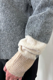 Close up view of the cuffs of a two toned gray sweater with beige in the cuffs turtleneck