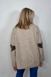 Back view of woman wearing a beige cardigan, v-neck and brown detailing with hearts in the elbows