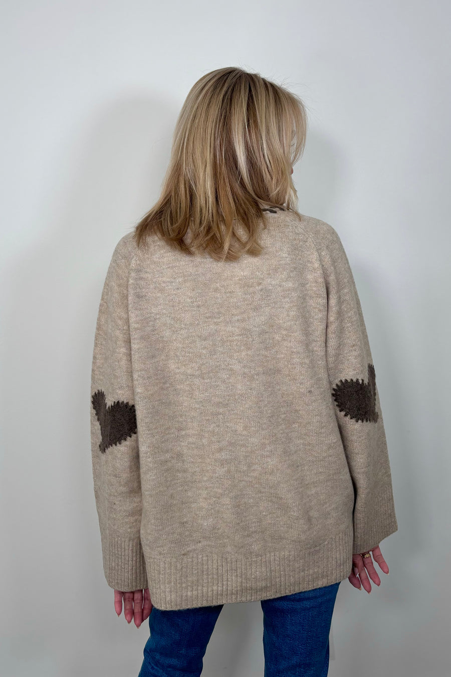 Back view of woman wearing a beige cardigan, v-neck and brown detailing with hearts in the elbows