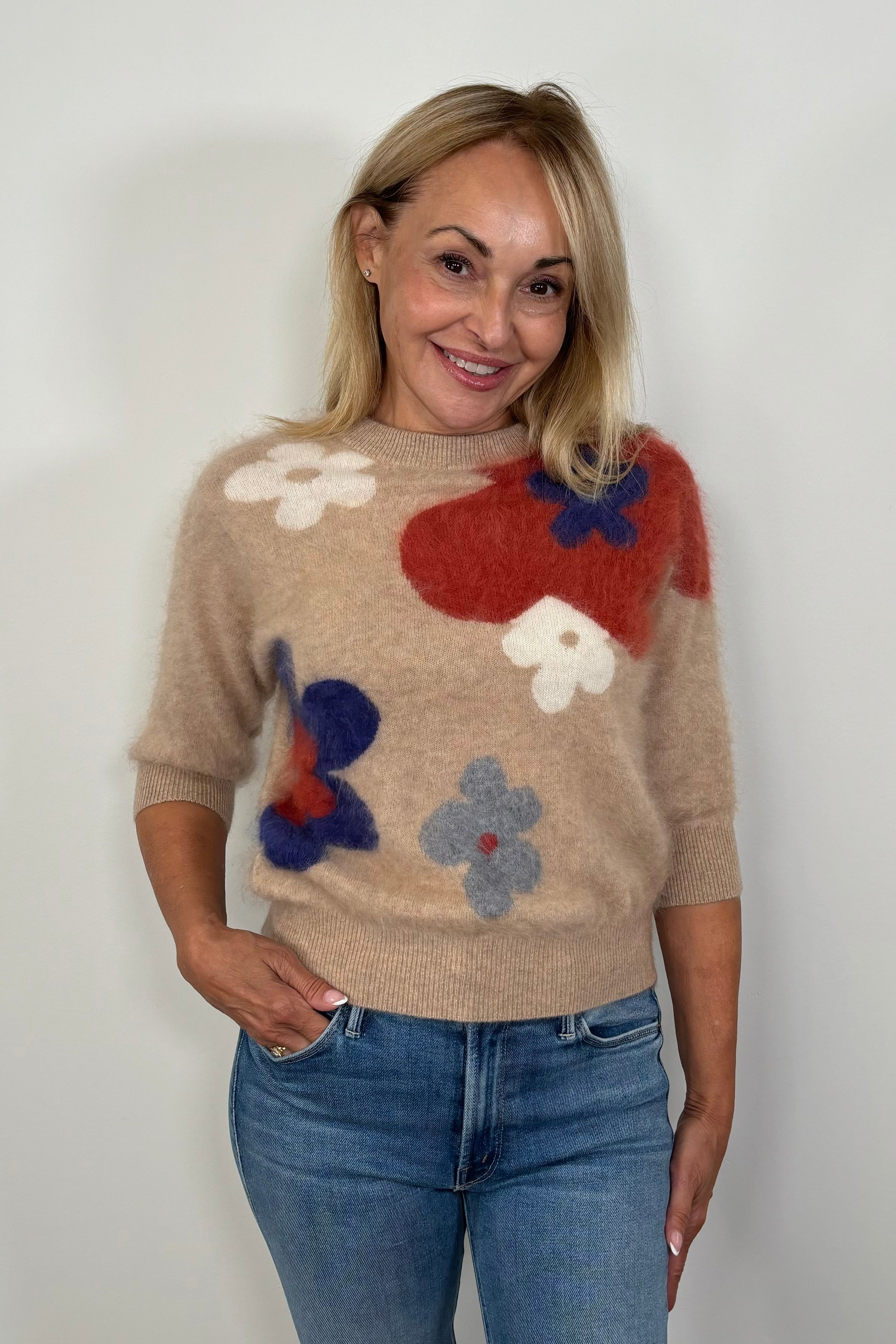 Front facing woman wearing a tan coloured with flowers 100% cashmere half sleeve sweater 