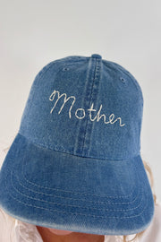 Close up of Woman wearing a light blue denim cap with “mother” stitched on the front