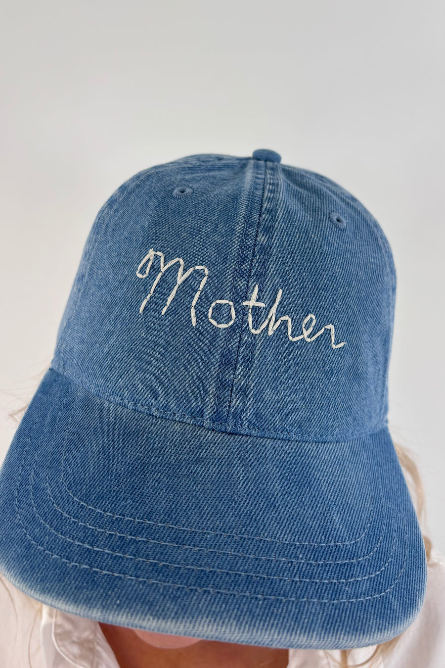 Close up of Woman wearing a light blue denim cap with “mother” stitched on the front