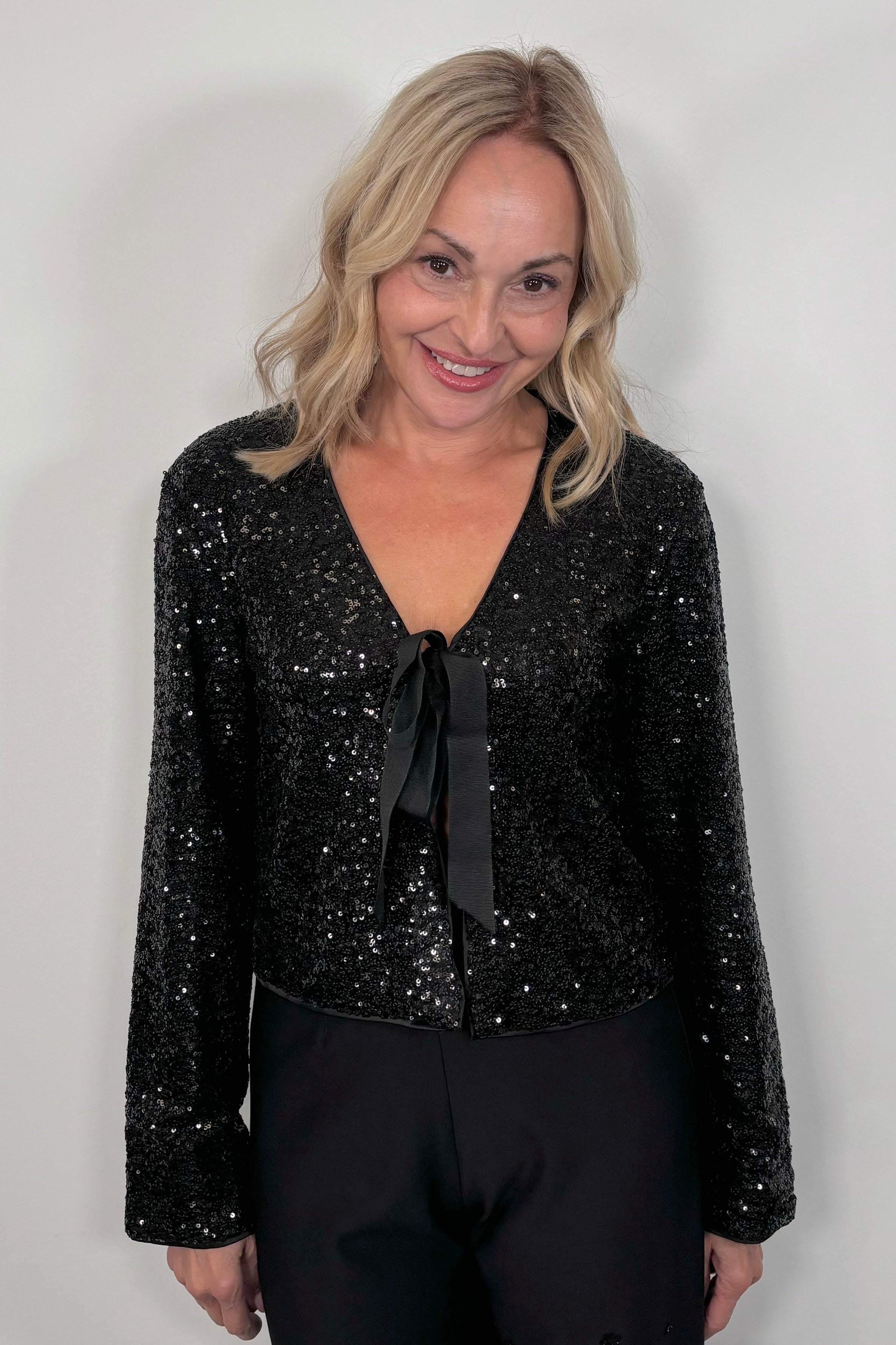 Woman wearing a black sequin cardigan with a bow tie against a white background