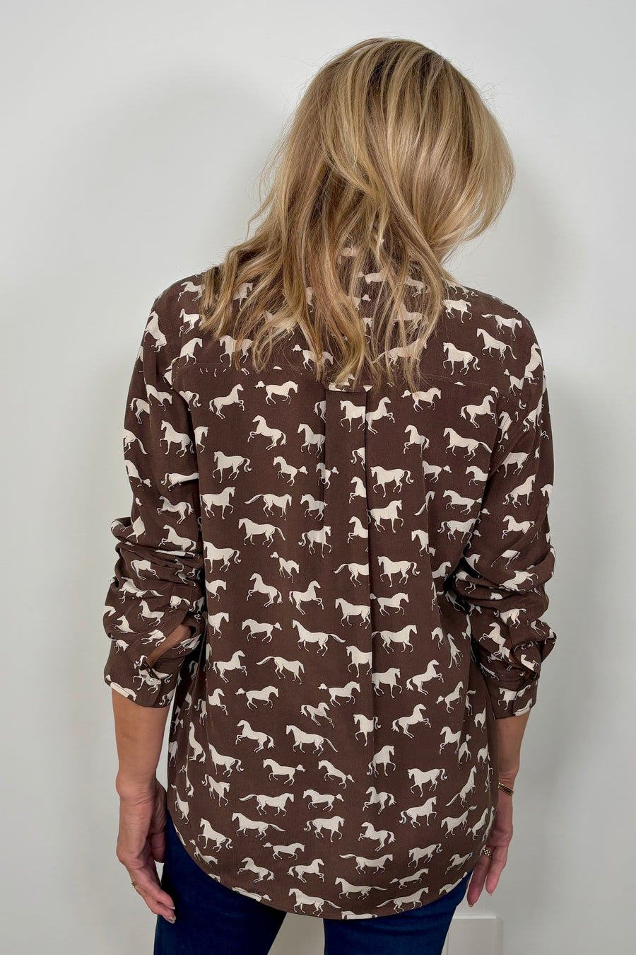 Back view of woman wearing a brown silk blouse with a white horse pattern all over 