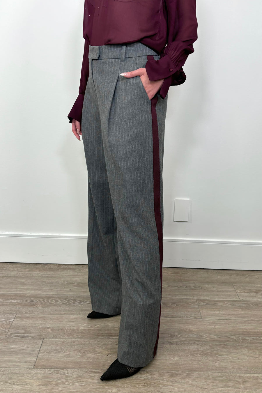 3/4 view of woman wearing a gray pinstripe wide leg pant with a burgundy line down the leg with hand in pocket