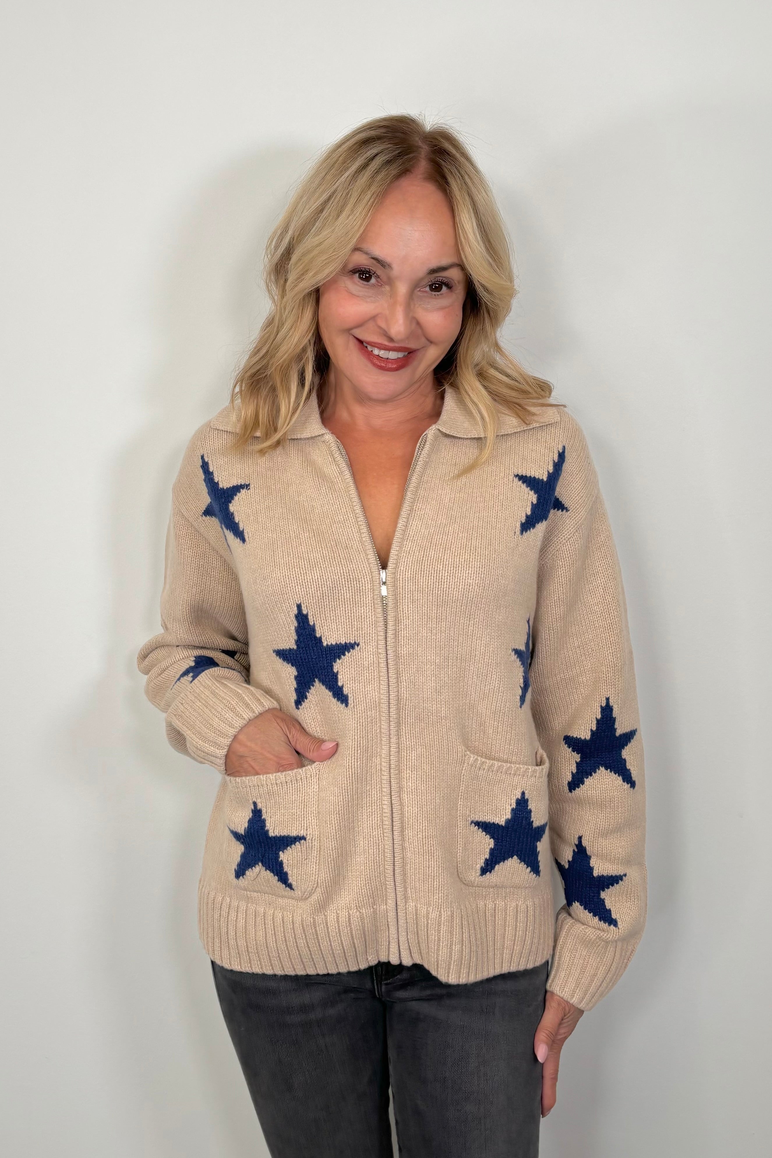 woman wearing a beige zip-up sweater with blue star patterns and front pockets