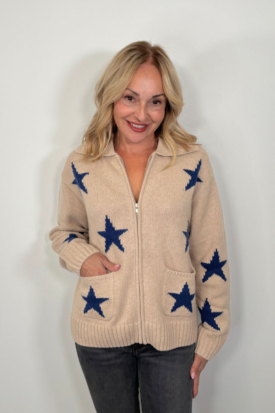 woman wearing a beige zip-up sweater with blue star patterns and front pockets