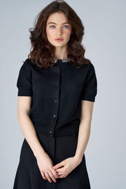 woman wearing a black cardigan with crystals in the collar with a skirt

