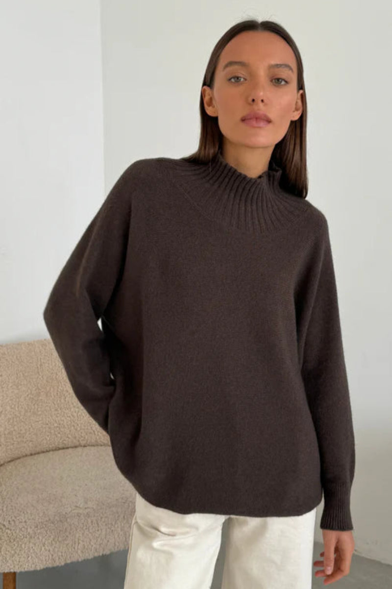 Woman wearing a brown sweater standing in a minimalistic room.