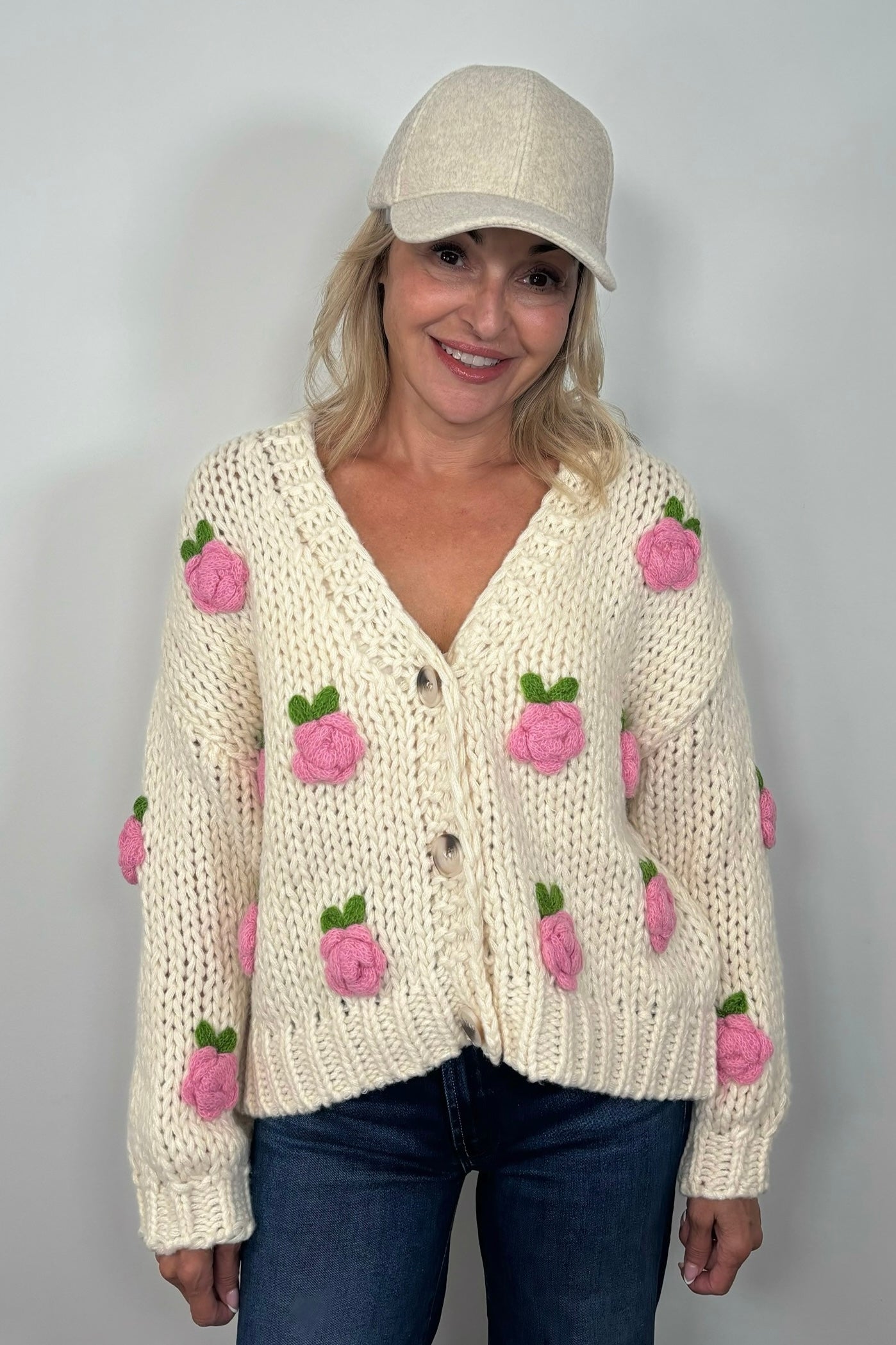 Front view of woman wearing an off white sweater with pink roses and a V-neck