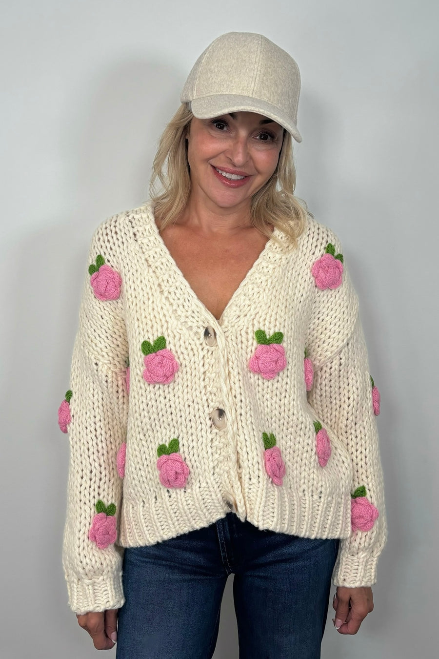 Front view of woman wearing an off white sweater with pink roses and a V-neck