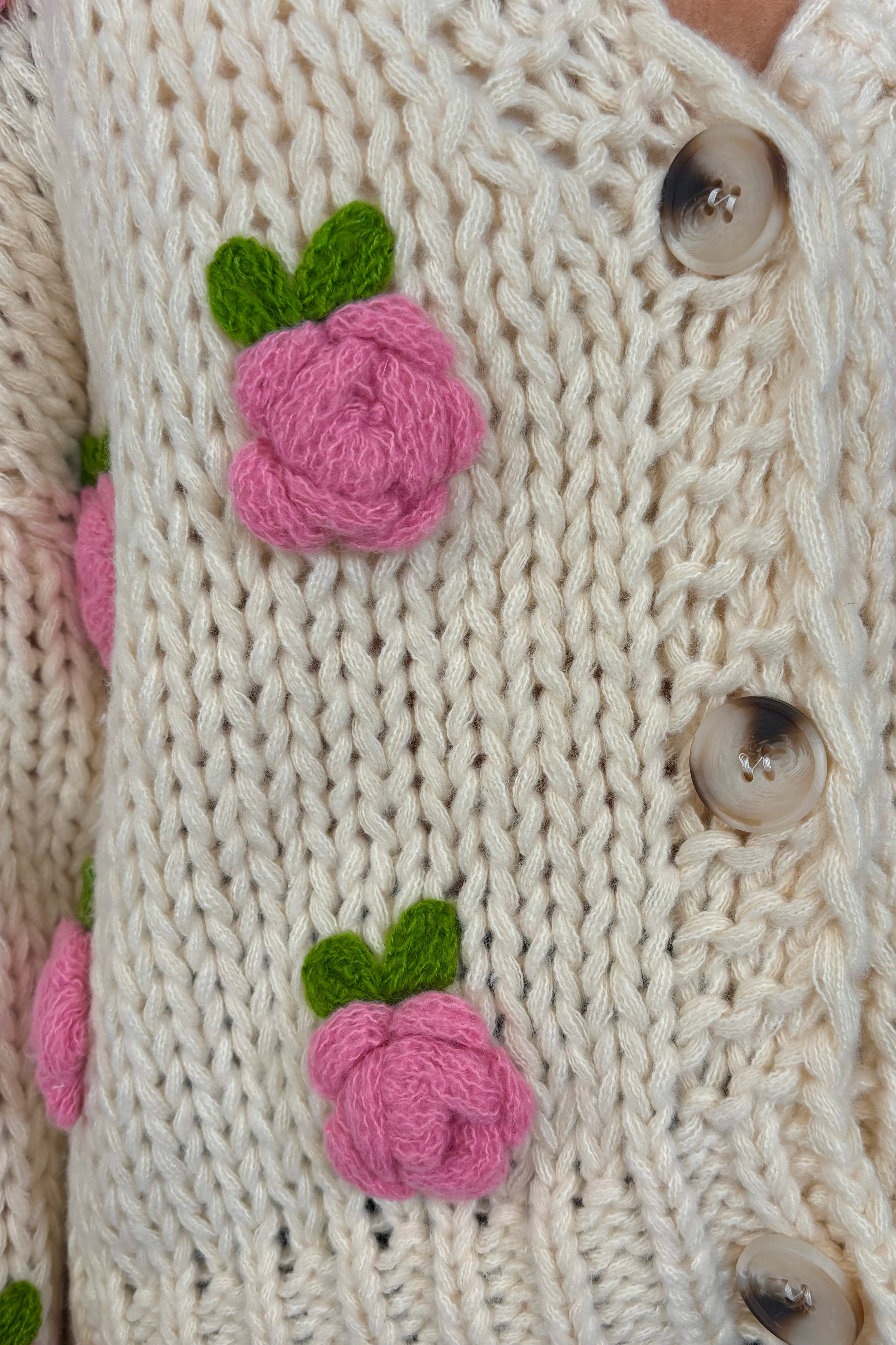 Zoom in view of woman wearing an off white sweater with pink roses and a V-neck