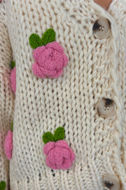 Zoom in view of woman wearing an off white sweater with pink roses and a V-neck