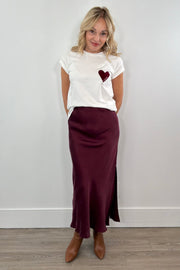 Woman wearing a white t-shirt with a heart design and a burgundy skirt against a plain background