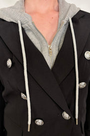 Close-up of a black blazer with silver buttons and a gray detachable hood.