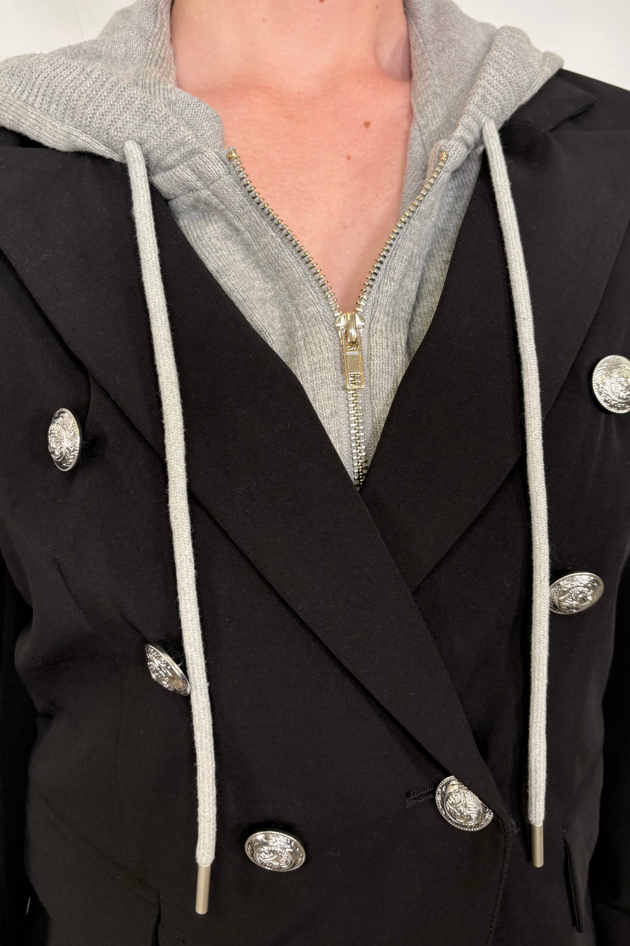 Close-up of a black blazer with silver buttons and a gray detachable hood.