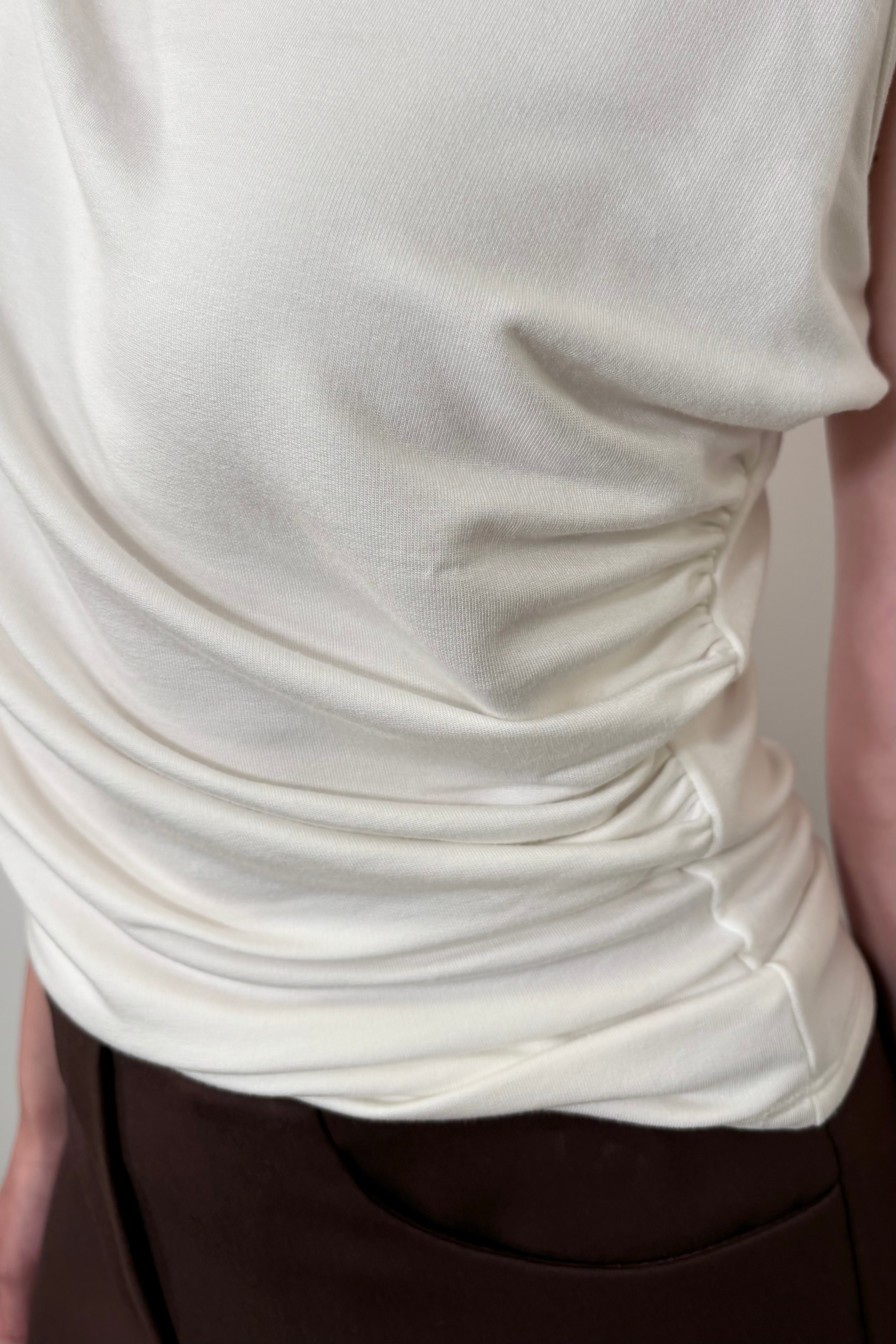 Zoom in of the rouching of a white sleeveless top a woman is wearing
