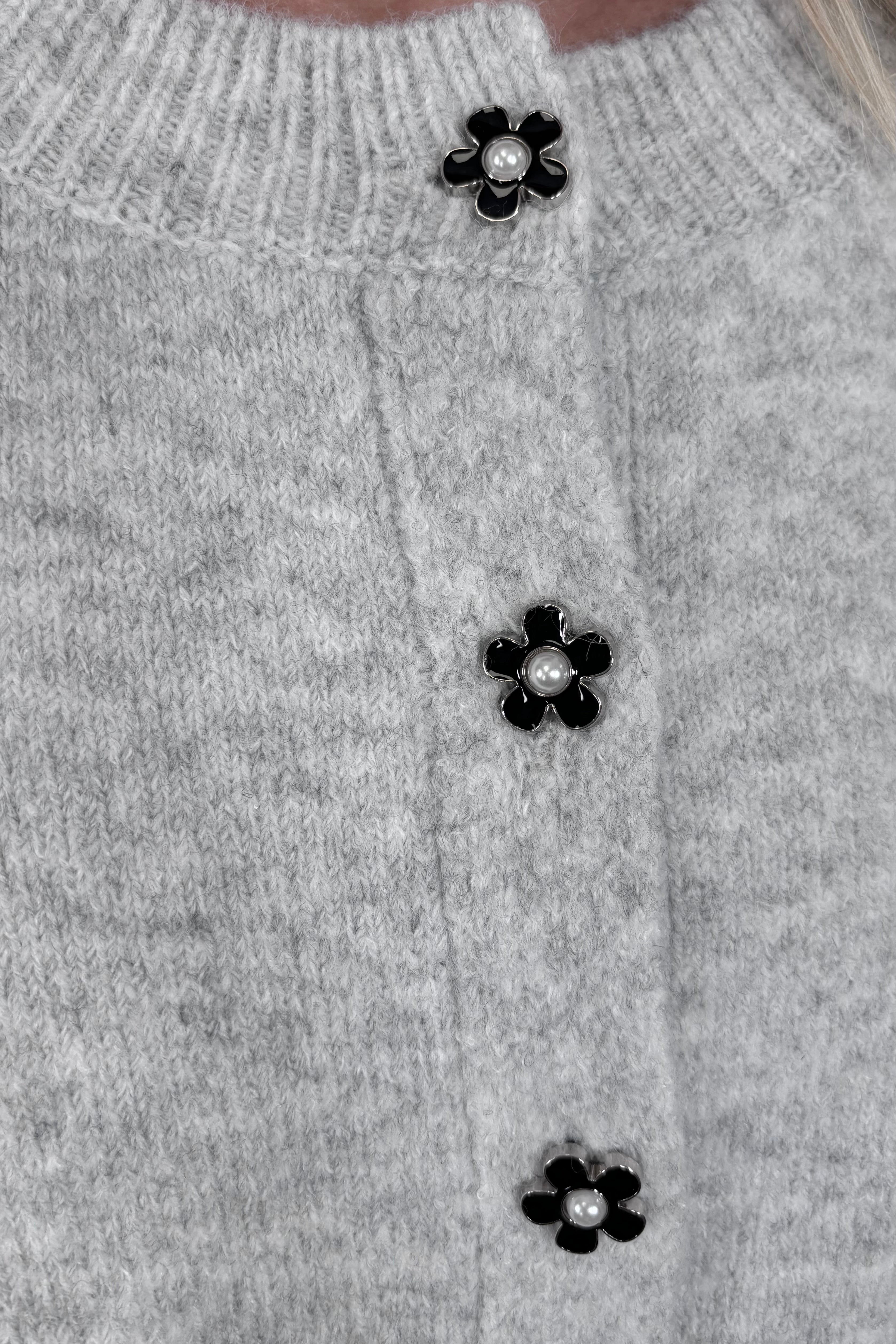 Zoom in view of woman wearing a gray cardigan with a black daisy pattern and buttons, done up
