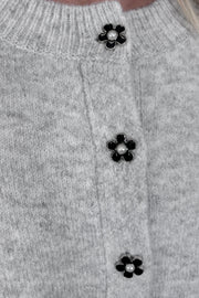 Zoom in view of woman wearing a gray cardigan with a black daisy pattern and buttons, done up