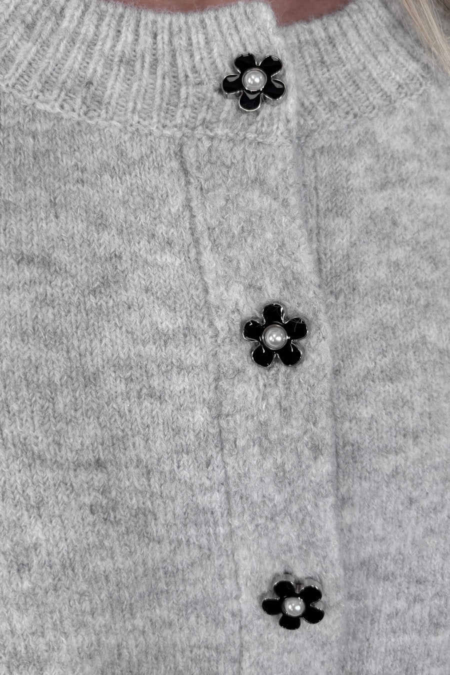 Zoom in view of woman wearing a gray cardigan with a black daisy pattern and buttons, done up
