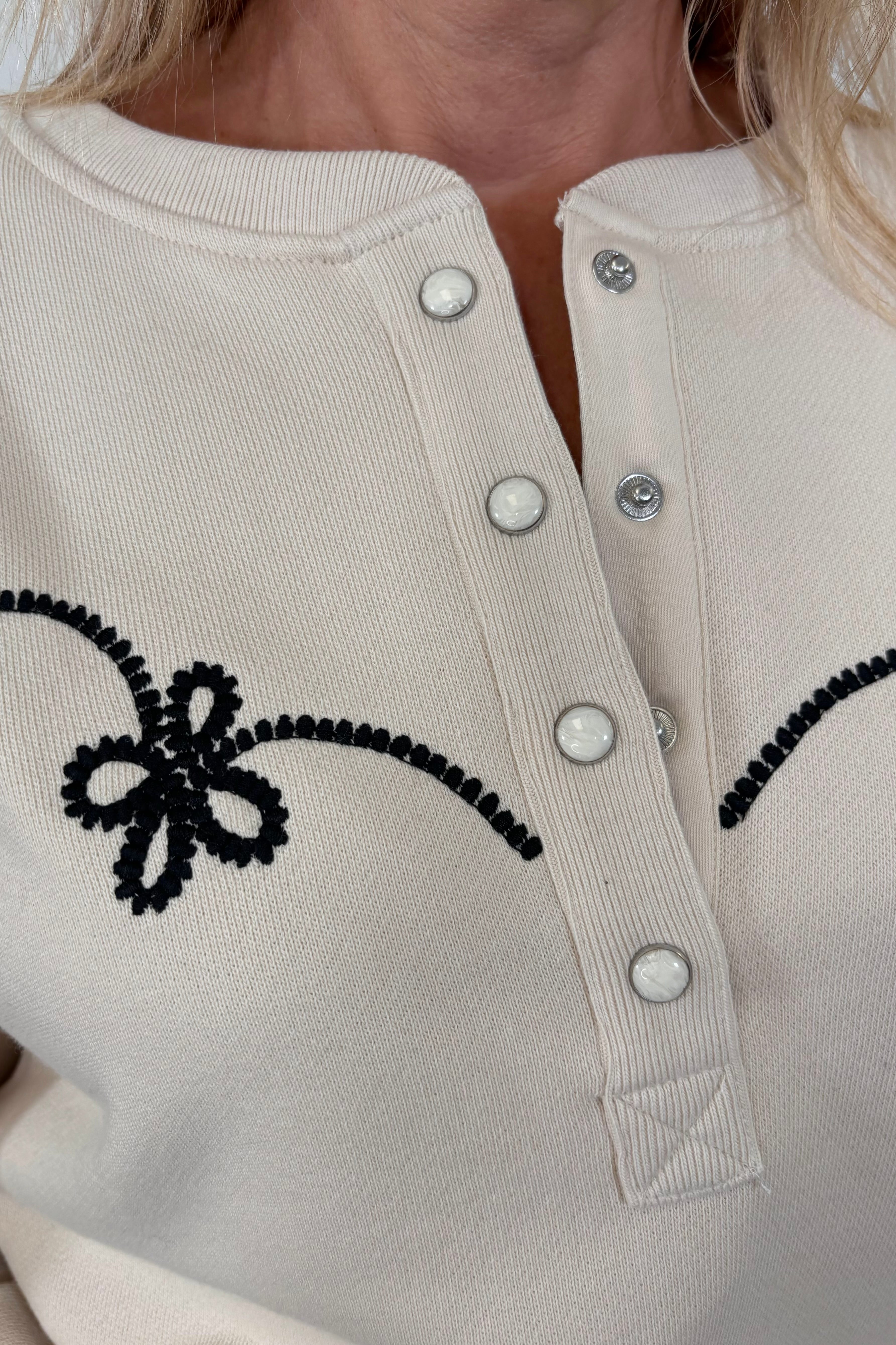 Zoom in of the Henley neck of a ecru coloured sweatshirt with western inspired detailing worn by a woman