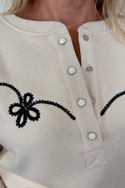 Zoom in of the Henley neck of a ecru coloured sweatshirt with western inspired detailing worn by a woman