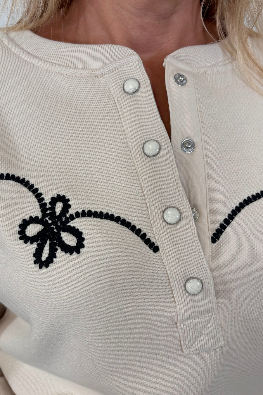 Zoom in of the Henley neck of a ecru coloured sweatshirt with western inspired detailing worn by a woman