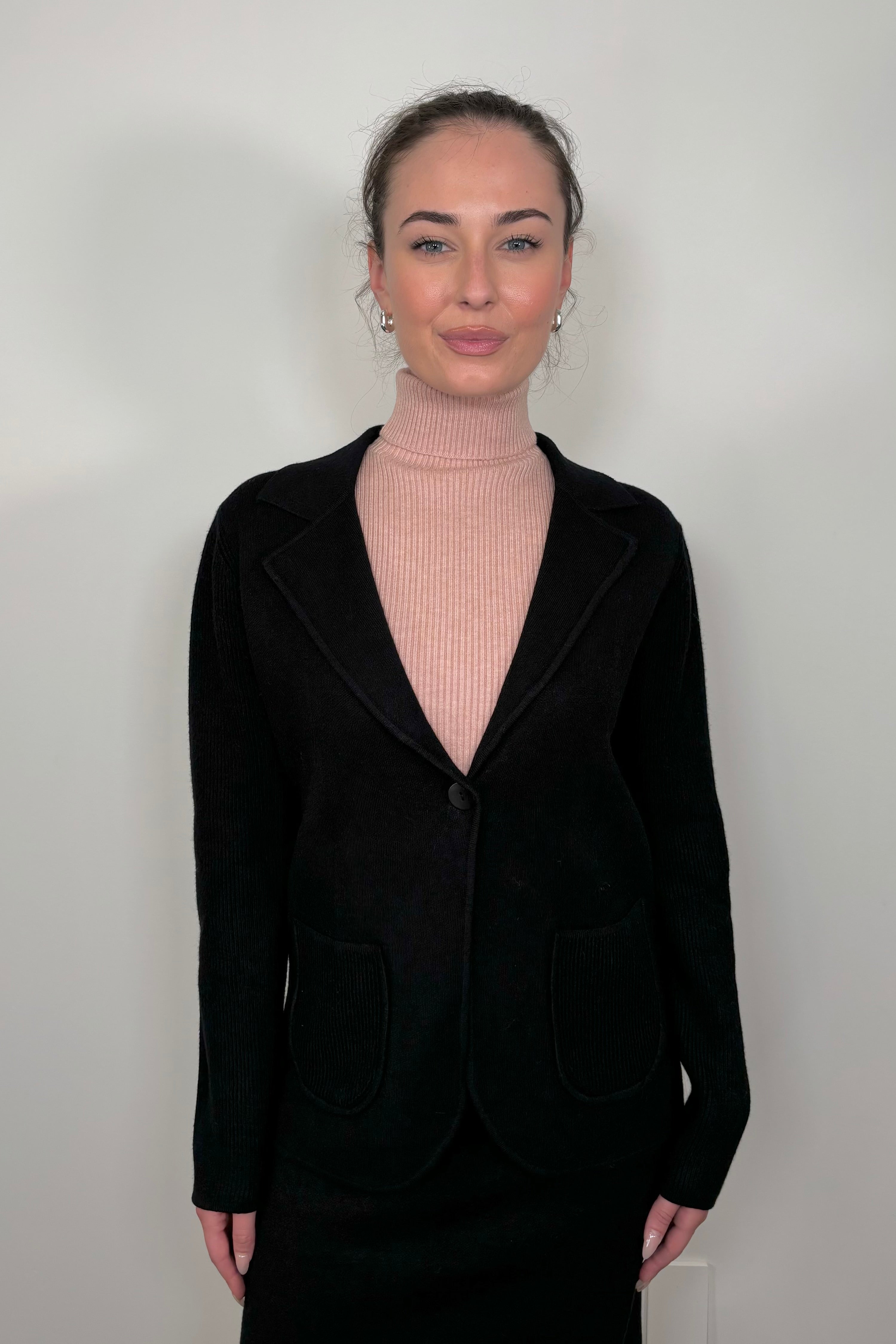 Front view of woman wearing a black knitted jacket and a pink turtleneck tank top