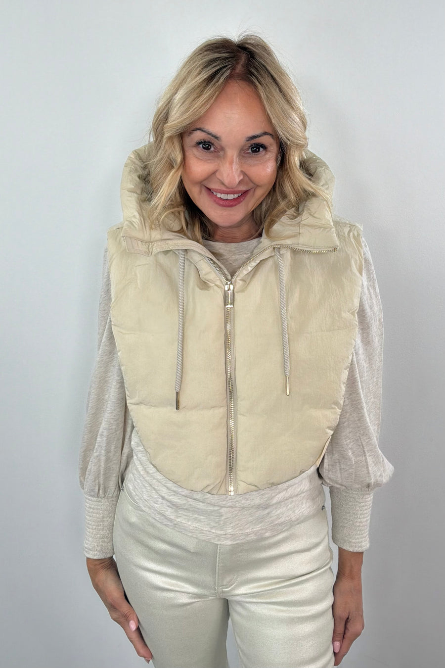 Woman wearing a beige puffer hood over a light-colored outfit against a plain background