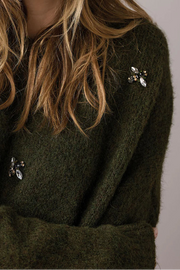 Woman wearing a green sweaater with decorative broches against a plain background