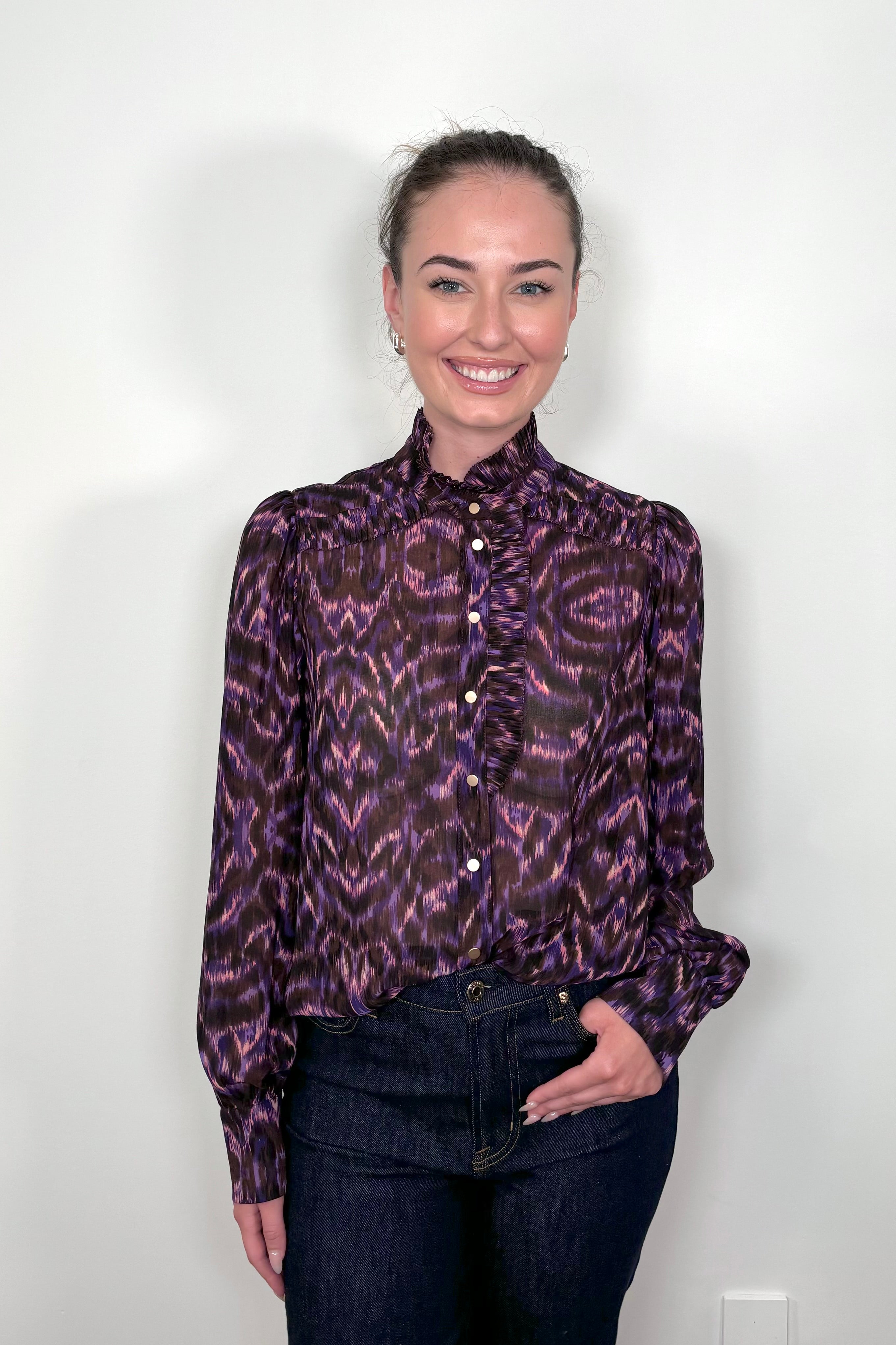 Front view of a woman wearing a violet sheer printed blouse with ruffles tucked in