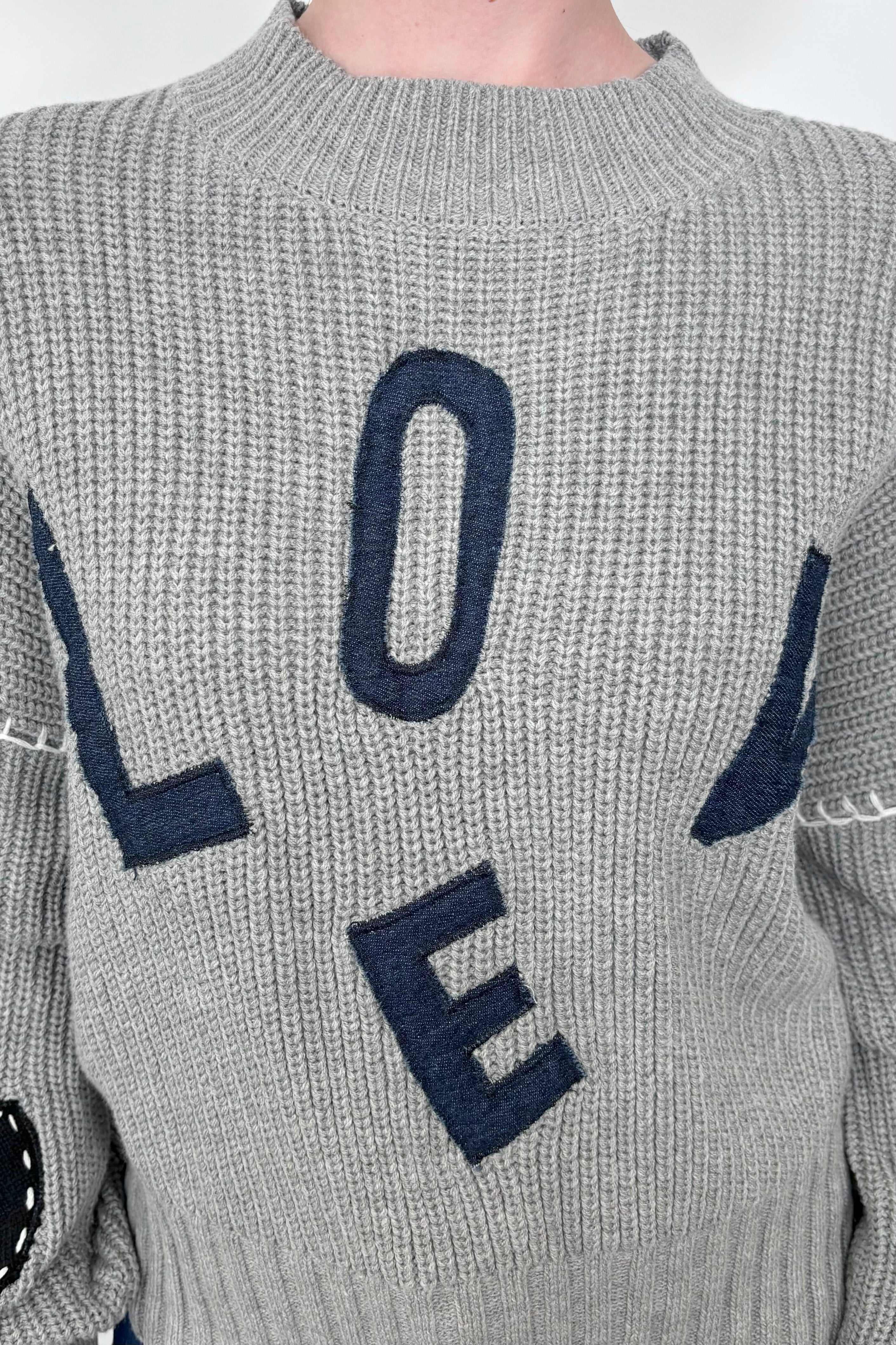 Close up view of a gray sweater with letter spelling love 