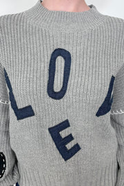 Close up view of a gray sweater with letter spelling love 