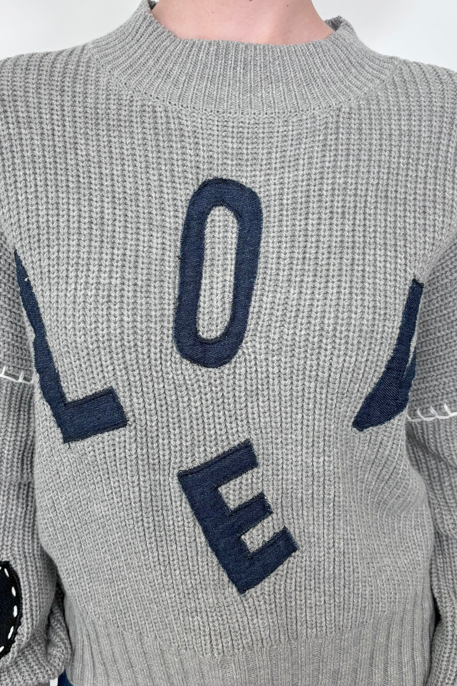 Close up view of a gray sweater with letter spelling love 