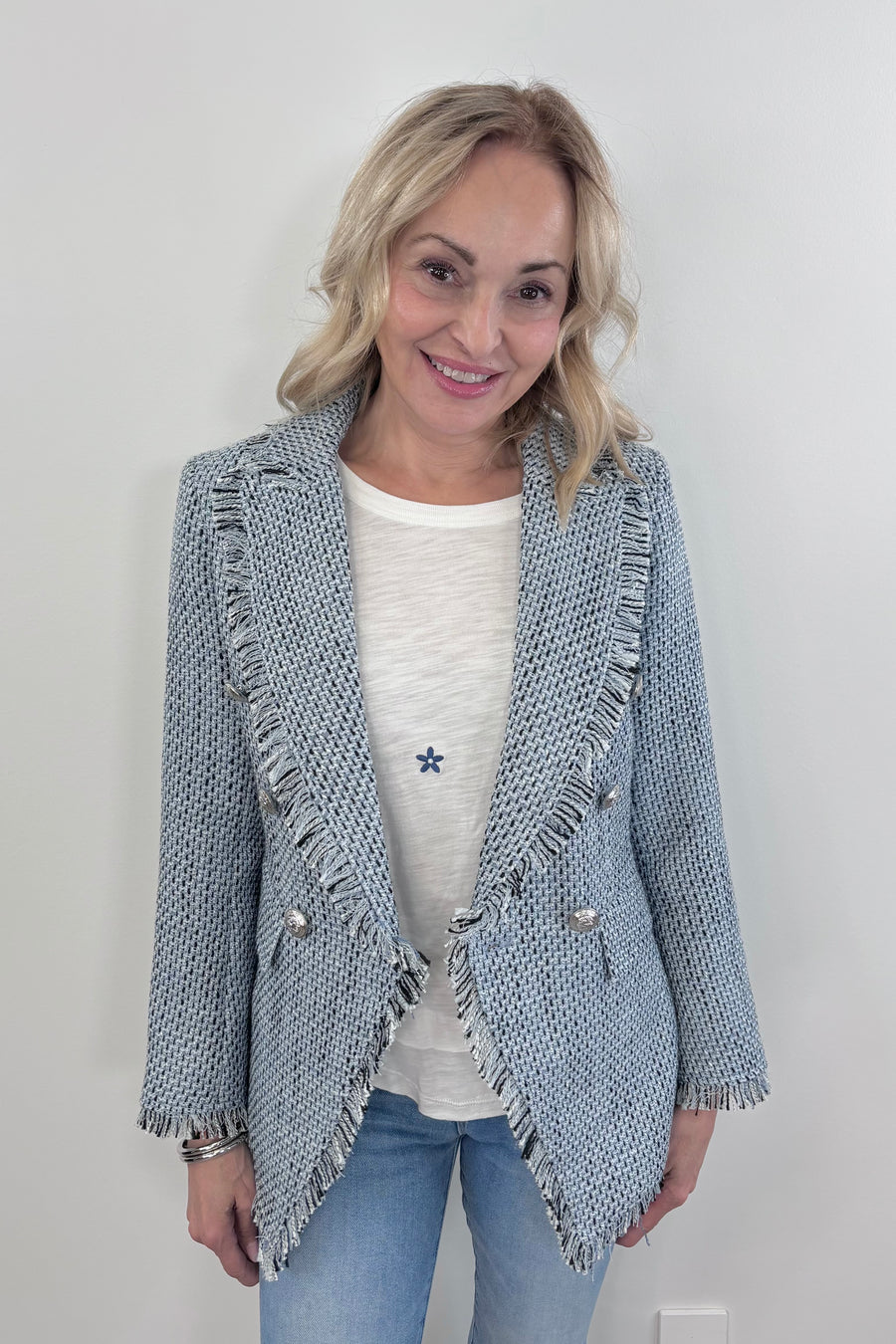 Woman wearing a light blue tweed blazer with silver buttons