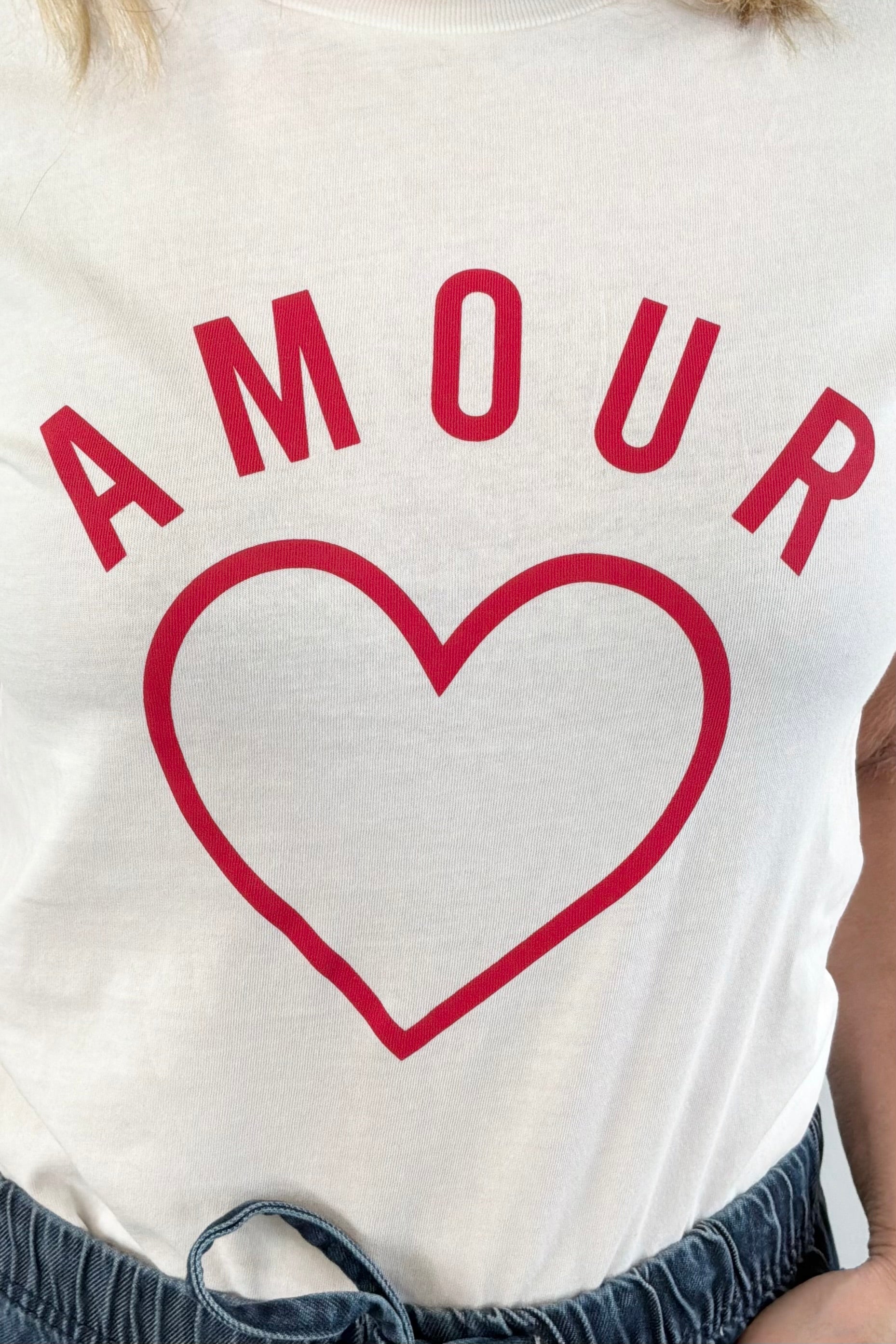 Closeup of Woman wearing a white crewneck t-shirt with the word "AMOUR" written in red lettering