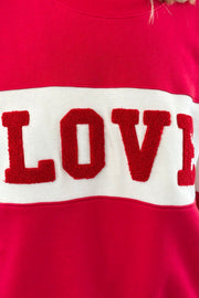 Closeup of Woman wearing wearing a red and off white color block crewneck sweatshirt with the word "LOVE" written in chenille