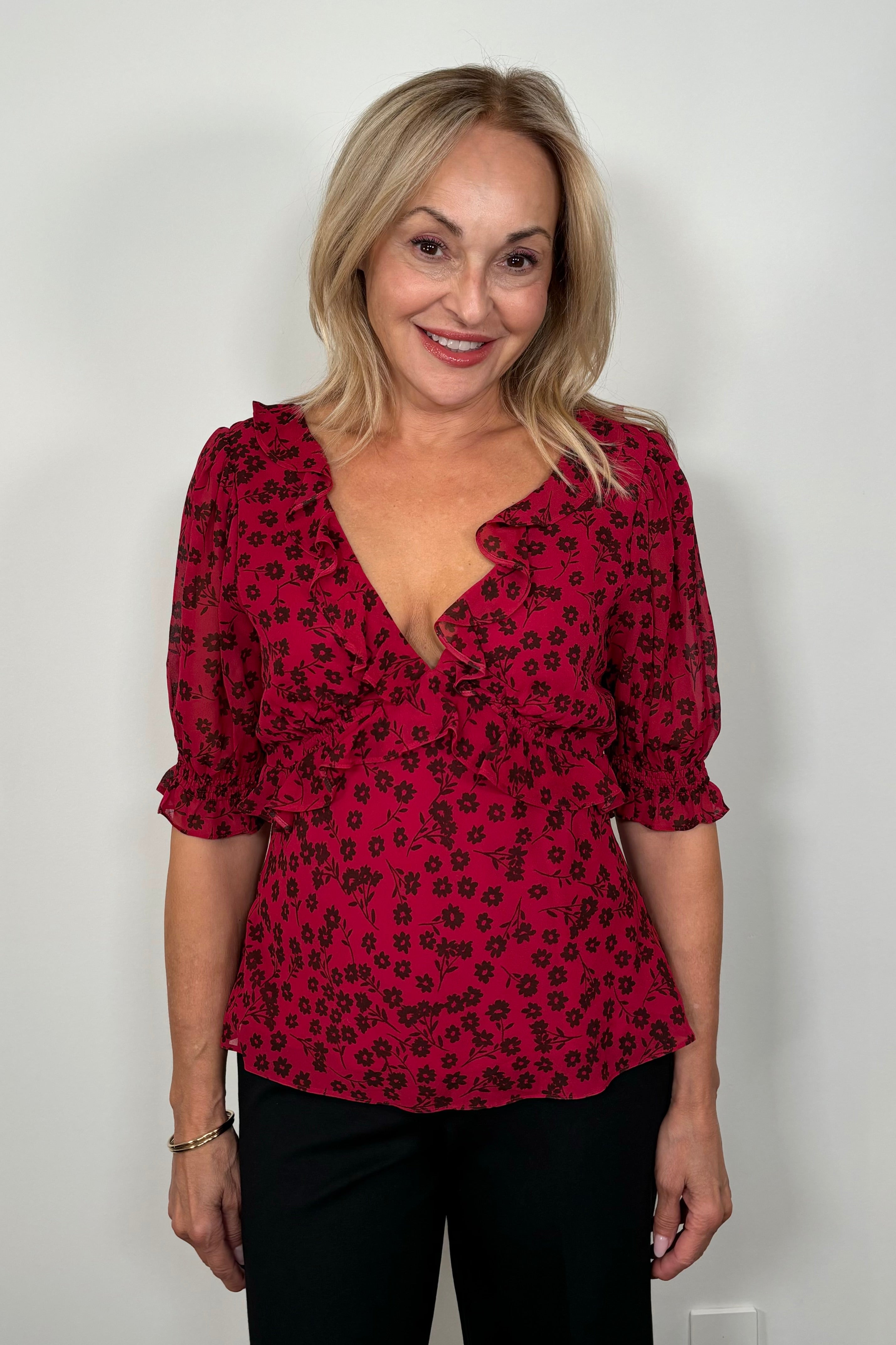Front view of woman wearing a cool red chiffon top with a daisy pattern