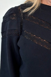 close-up of a black sweatshirt with lace detailing and cuffed poplin  sleeves