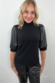Woman wearing a black mix media turtleneck top with leather half sleeves.