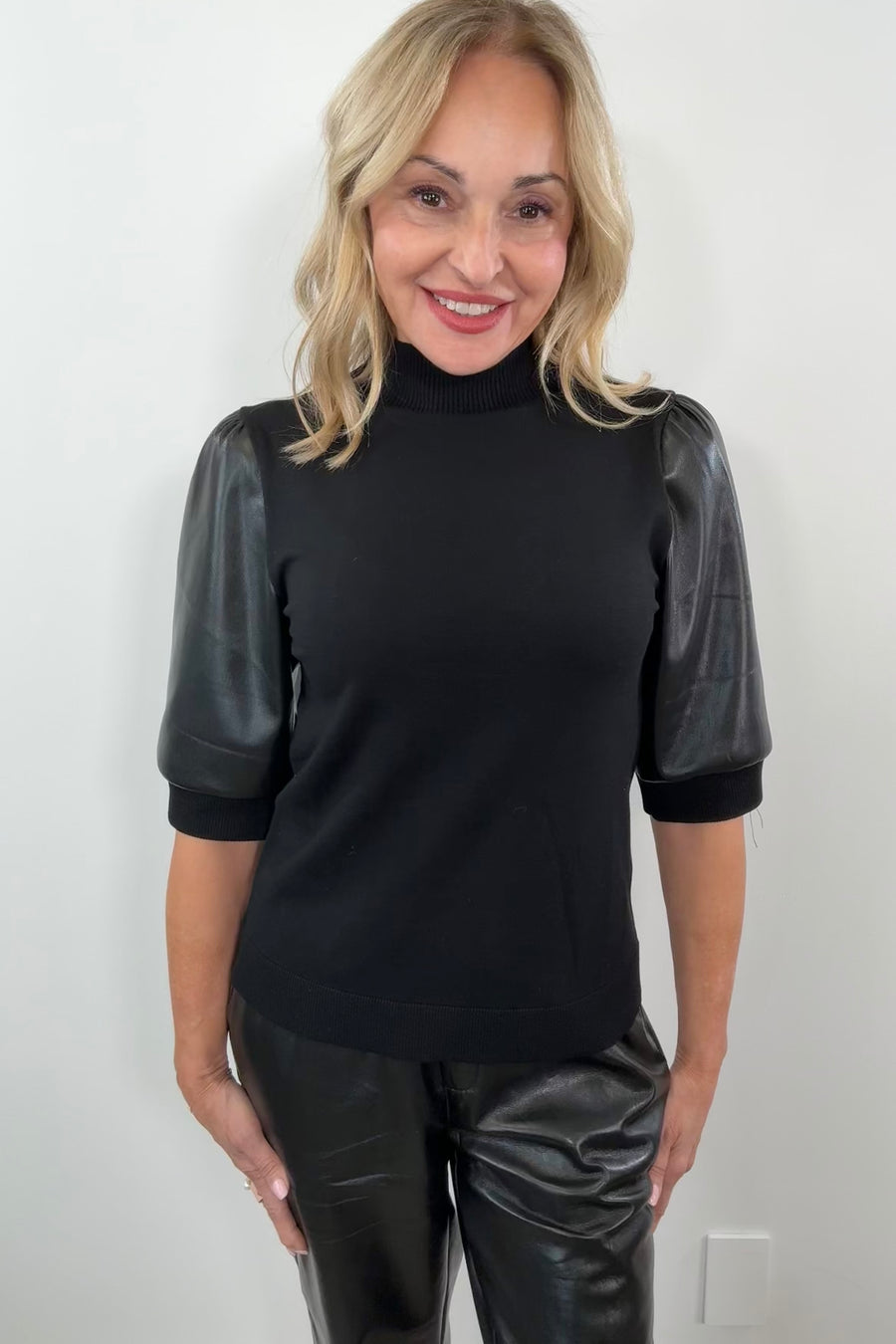 Woman wearing a black mix media turtleneck top with leather half sleeves.