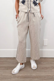 Woman wearing cream linen drawstring pants with contrast embroidery along the sides, front view