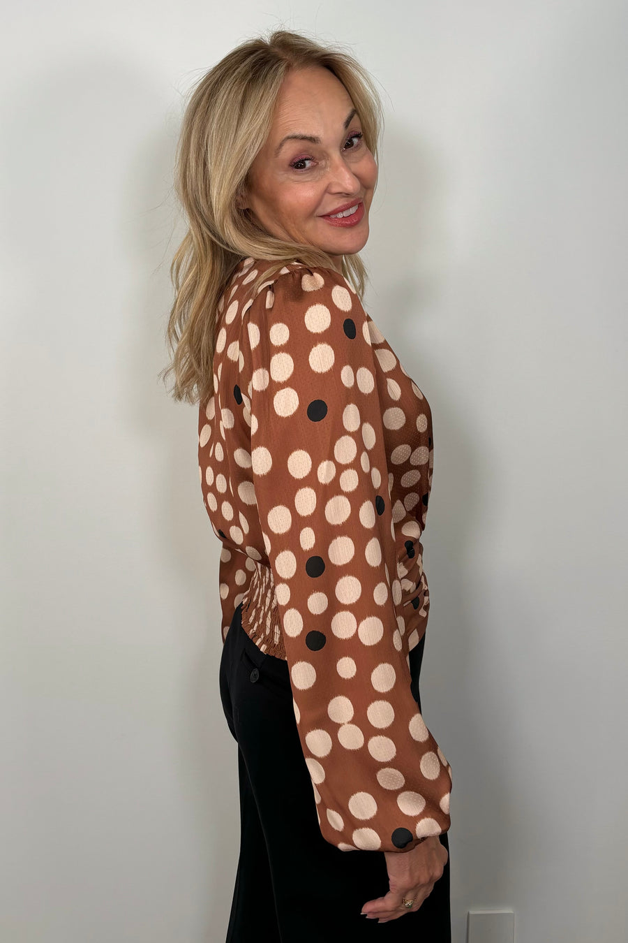 Side view of woman wearing a dusty warm brown top with bicolored dots, soft puff sleeves and wrap front