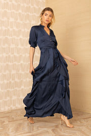 Side view of woman wearing a silk v-neck navy blue dress with ruffles
