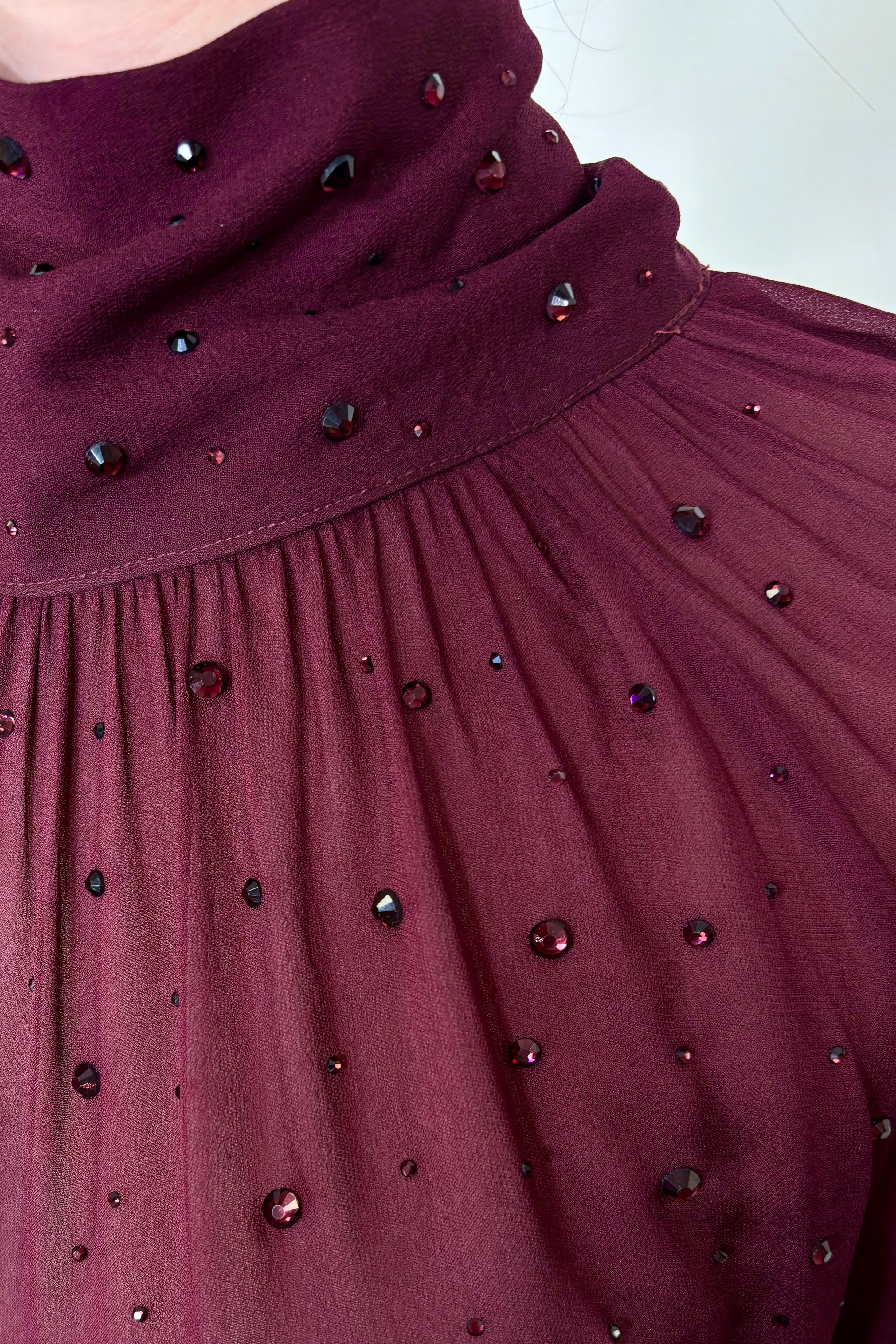 Close-up of woman wearing a burgundy mesh long sleeve top with crystal embellishments 