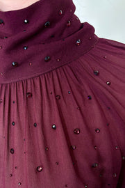 Close-up of woman wearing a burgundy mesh long sleeve top with crystal embellishments 